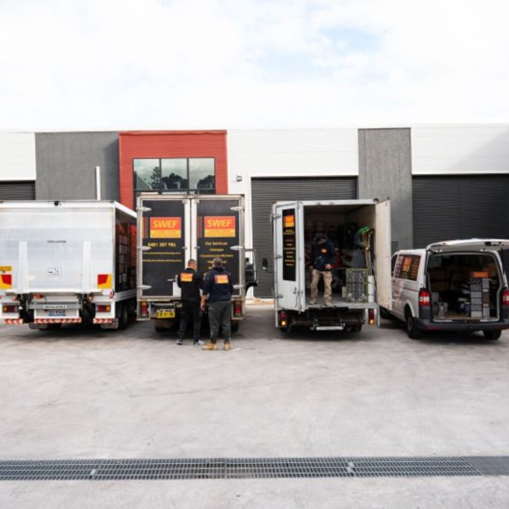 Three men showcasing epoxy flooring for garages in Sydney outside a large warehouse.