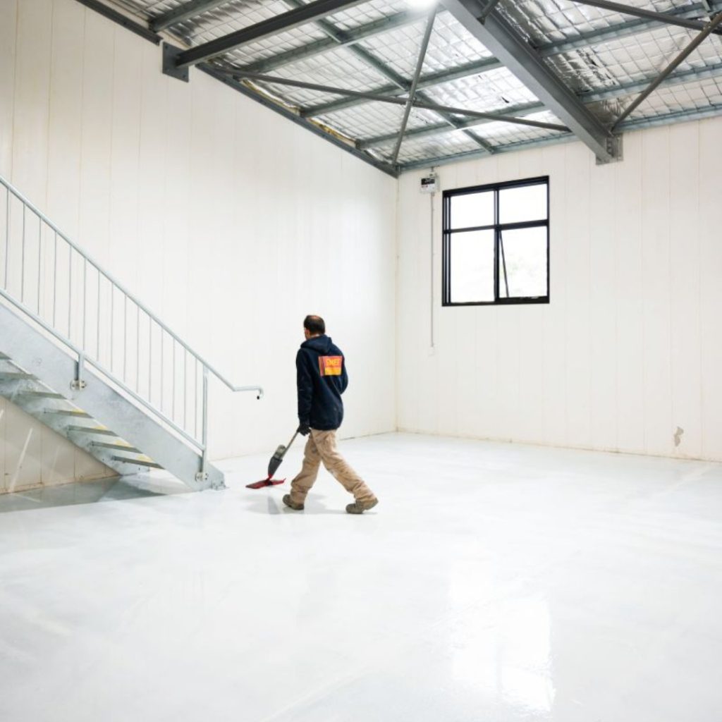 A man walks through an empty workshop space with epoxy flooring, showcasing a spacious and clean workshop environment in Sydney.