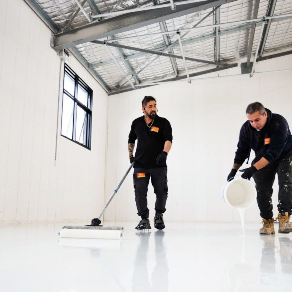 Two men diligently applying commercial epoxy floors in Sydney to a commercial building, showcasing professional installation and quality workmanship.