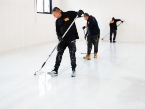 Team applying epoxy coating to a warehouse floor, demonstrating the long-lasting durability of epoxy flooring.