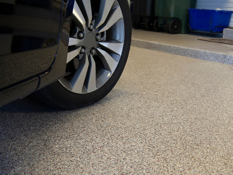 Car parked on a garage floor with a shiny epoxy coating, showcasing the durability and aesthetics of epoxy coating on floors.