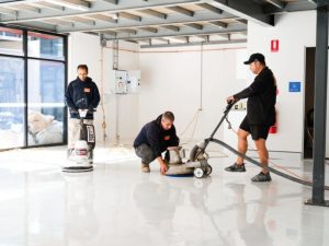 Workers polishing an epoxy floor to repair and remove visible epoxy floor scratches in a commercial space.