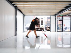 Worker applying epoxy resin floor coating in a commercial space to ensure a durable, glossy finish.