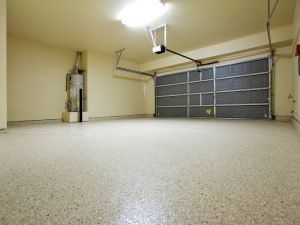 Epoxy floor cracking in empty garage with water heater in the corner, highlighting durability issues.