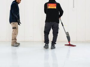 Technicians inspecting and finishing an epoxy resin floor installation in an indoor commercial setting.