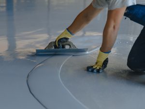 Close-up of worker using a trowel to spread self-levelling epoxy coating types on a concrete floor.