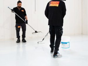 Workers applying epoxy floor coating in a storage warehouse. Floor storage warehouse being prepared for durability.