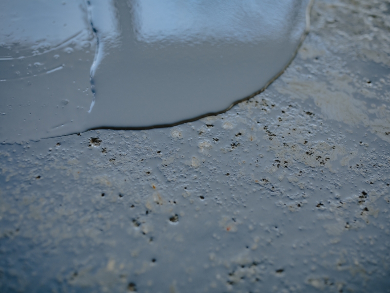 Close-up of liquid epoxy poured over a rough concrete surface, showing factors affecting epoxy floor costs.