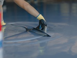 A worker using a trowel to spread epoxy resin on a floor, illustrating professional installation's impact on epoxy floor costs.