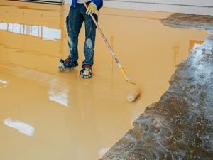 A man applying the best type of epoxy flooring to a high-traffic garage floor for durability.