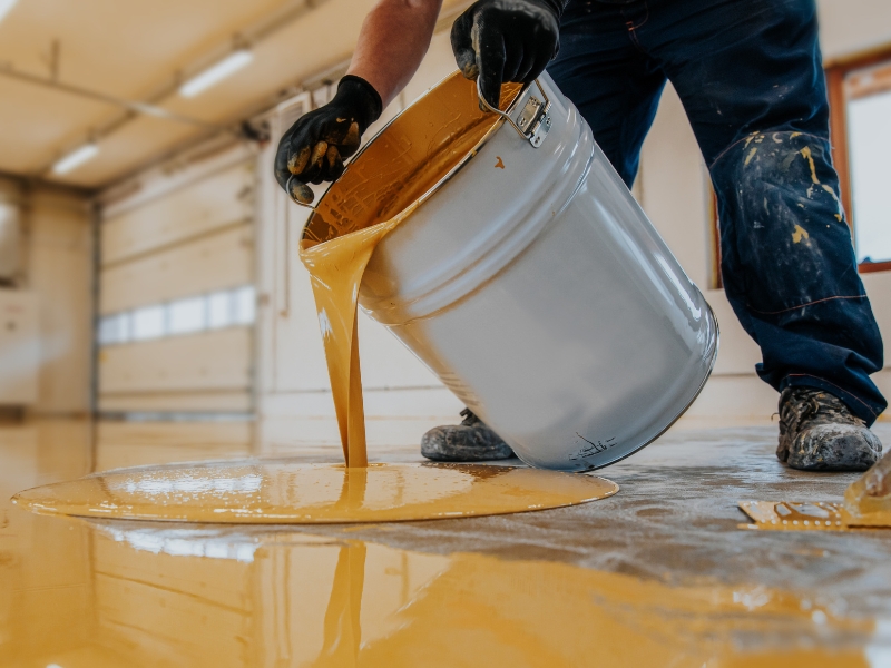 A man applying a type of epoxy flooring coating to a high-traffic garage floor for durability.