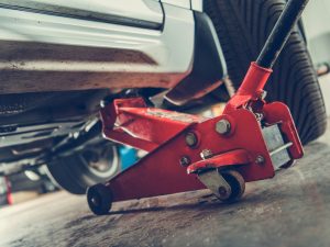 A red floor jack is used to lift a car on uneven floors.